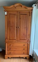 Front view of the pine armoire showing the closed double doors, two bottom drawers, and ornate top edge.