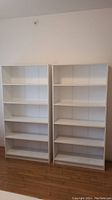 Two white IKEA bookshelves side by side against a wall on a hardwood floor.