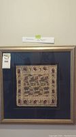 Framed silk woven art featuring square textile with animal motifs, including elephants and birds, mounted on dark blue matte in a decorative gold frame.