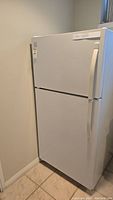 Front and angled view of white Kenmore top freezer refrigerator placed in basement corner against walls and tile floor.