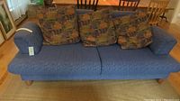 Front view of blue fabric ScanDesigns sofa with removable armrests and loose patterned cushions.