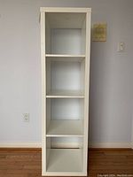 Front view of tall white IKEA shelf unit showing three shelves.