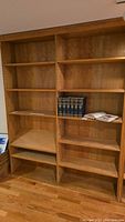Front view of two adjoining wood bookcase modules with multiple adjustable shelves, a set of books on one shelf.