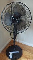 Front view of black Honeywell standing floor fan on wooden floor against beige wall