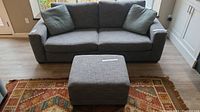 Grey fabric sofa with two seat cushions, two back cushions, and two green accent pillows. Straight arms and modern style visible from front view.