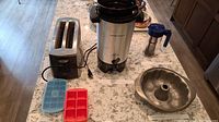 Overview of lot contents showing Breville toaster, Hamilton Beach coffee urn, baking pan, two silicone ice cube trays, and Takeya iced tea brewer on kitchen counter
