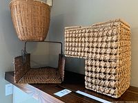 Three wicker baskets displayed on a shelf: a round basket, a square basket with metal frame, and a staircase-shaped basket.