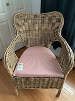 Front view of wicker chair with red and white striped cushion on wooden floor near white doors.