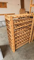 Angled view of the wooden wine rack showing multiple bottle slots and side supports in a garage or storage room.