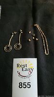 Overhead shot of all jewelry items on black background including rope chain, dangle earrings, stud earrings, earring backs and lot number card