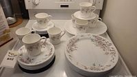 Lot showing 4 floral patterned cups and set of plates, along with an oval floral platter on a stove surface.