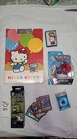 Full view of all items displayed on white surface including Hello Kitty clipboard, keychain, Pokémon toy, Yu-Gi-Oh cards, and Nightmare Before Christmas figures.