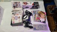 Full lot showing Vogue Knitting magazines stacked near a handheld clothes steamer and boxed handheld vacuum cleaner.