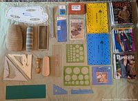 Overview of all sewing and knitting tools, pattern drafting templates, knitting needles, shoe horn, a box labeled shoe strings, and multiple issues of Threads magazines arranged on beige surface.