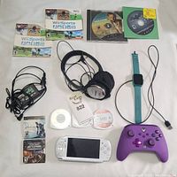 All items together on a white cloth showing the full lot including games, PSP, headphones, smart watch, controller