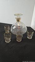 Photo of the full set showing vintage glass decanter with stopper and four matching glasses arranged on a black surface.