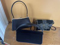 Photo showing three evening bags: a small black handbag with metal frame and clasp, a black velvet clutch, and a black beaded bow decorated evening bag.