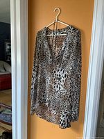 Leopard print tunic hanging on white hanger showing front side with v-neck and long sleeves.