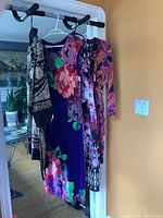 Four dresses and one tunic hanging on a doorway, showing variety of prints and colors including paisley and floral