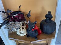 Shows the full Halloween decor lot with the floral skull, black rodent figurine in red cape, and raven on pumpkin display all arranged on corner shelf.