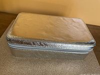 Closed silver rectangular jewelry travel box with metallic texture and zipper closure.