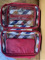Opened cosmetic bag showing multiple clear vinyl zippered pockets and colorful plaid fabric interior.
