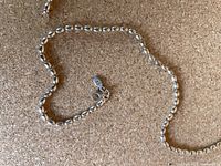 Full length view of the silver bead chain necklace laid flat showing bead design and clasp with marking tag visible.