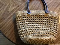 Photo showing the exterior natural and yellow woven texture with brown handles of the tote bag.