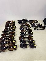20 pairs of magnified sunglasses arranged side by side on a surface, showing tinted lenses and black frames with magnification stickers.