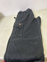 Folded black Dickies cargo pants showing side cargo pocket with flap and Dickies logo patch.