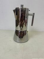 Full view of the stainless steel stovetop espresso maker showing the cylindrical top chamber, wide base, handle, and spout.