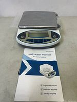 Full view of digital electronic balance scale with stainless steel platform and instruction manual on display.