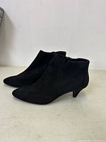 Side profile photo of black suede ankle boots with pointed toes and kitten heels on a white surface.