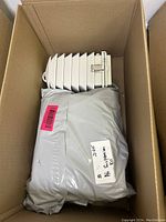 White electric space heater and two gray sealed packages inside a cardboard box, viewed from above.