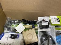 Top view of box showing assorted miscellaneous items including Dixon auto part, black sunglasses, packaged small parts, personal heater remote control, and other items