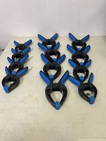 12 Tool Tech firm grip clamps arranged neatly on a white surface, showing black plastic body and blue tips.