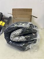 Photo of folded Miguel pet bed in clear plastic packaging with cardboard box behind it.