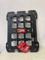 Image of black Milwaukee Packout mounting plate with multiple square cutouts and mounting holes, showing item's structure and material.