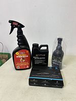 Wide view of lot showing all four items on table: spider killer spray, Archoil Friction Modifier, Archoil Diesel Fuel System Cleaner in plastic, and radar detector box.