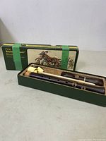 Recorder laid in original green box with decorative lid showing artwork and minor damage, wooden cleaning rod with yellow felt included.