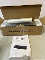 Open cardboard box containing OL168 A4 Laminator with protective packaging and visible roller.