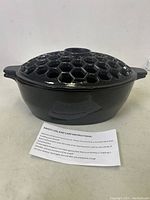 Front view of Plow & Hearth black cast iron steamer with lattice lid and accompanying care instructions.