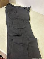 Photo showing black cargo pants folded, highlighting the cargo pocket and fabric texture.