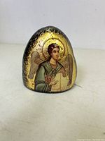 Front view of oval river-washed stone with Byzantine saint icon print on gold-glided surface