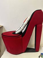 Side view of red high heel shoe chair showing shape and lipstick pillow on backrest.