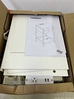 Unassembled white side table parts in open box with visible integrated power unit and instruction manual for model 72UBZ01.