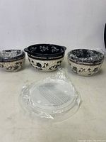 Front view of three ceramic bowls with black and beige floral woven basket design, two smaller and one larger bowl, wrapped in plastic