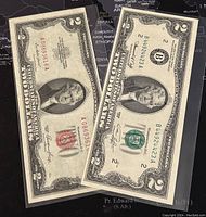 Two US $2 paper banknotes in plastic sleeves, one with red seal from 1953 series and one with green seal from 1976 series.