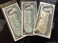 Three Canadian one dollar banknotes from 1954, 1967, and 1973 in protective sleeves displayed on a black map background.