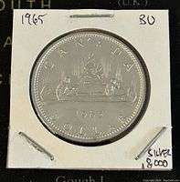 Image of the reverse side of a 1965 Canadian Silver 1 Dollar coin in BU condition showing canoe design and inscriptions.